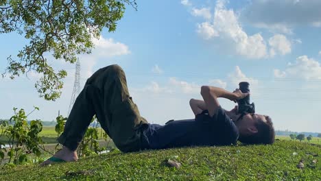 Man-lying-on-grass-ground-taking-pictures-of-clouds-in-the-sky,-zoom-out,-day