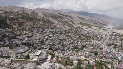 Drone-flyover-Gjirokaster-cityscape-with-massive-mountains-in-Background,-Albania