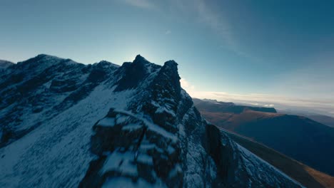 Cinematic-drone-flight-along-snowy-summit-of-Norwegian-mountains-during-lighting-sunrise-in-background---FPV-flight