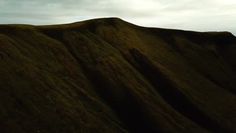 Luftlandschaftsansicht-Der-Dunklen-Berge-Des-Isländischen-Hochlandes,-Bedeckt-Mit-Hellgrünem-Gras,-An-Einem-Bewölkten-Tag