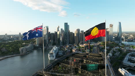 Bandera-De-Australia-Y-Bandera-Aborigen-En-La-Parte-Superior-Del-Puente-Del-Puerto-De-Sydney-Con-Vista-Panorámica-Del-Horizonte-De-Cbd-En-Sydney,-Australia