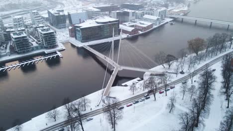 Circling-around-a-beautiful-pedestrian-bridge-over-the-river-Drammenselva-in-town-of-Drammen,-Norway-during-snowfall