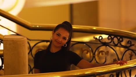 Young-Charming-Beautiful-Brunette-Lady-Model-Smiling-Looking-at-Camera,-Next-to-Luxury-Indoor-Stair-Railing