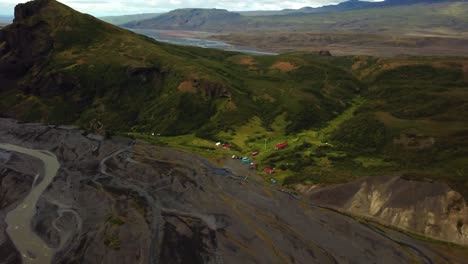 Aerial-view-over-a-river-flowing-through-a-valley,-next-to-a-colorful-village,-in-FimmvÃ¶rÃ°uhÃ¡ls-area,-Iceland