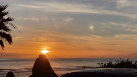 Silhouette-of-huge-sunset-with-woman-takes-photos-or-video-at-sunset-on-the-carcavelos-beach