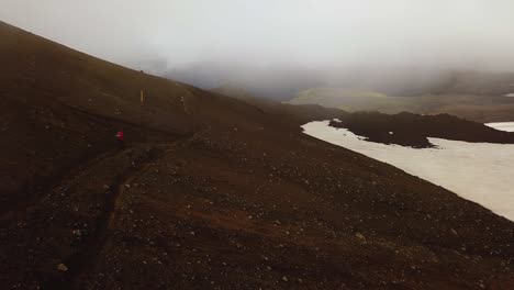 Aerial-landscape-view-of-a-person-hiking-on-a-mountain-trail,-on-a-foggy-day,-Fimmvörðuháls-area,-Iceland