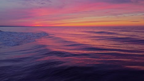 Sea-waves-rolling-and-reflecting-orange-sunset-sky,-low-altitude-aerial