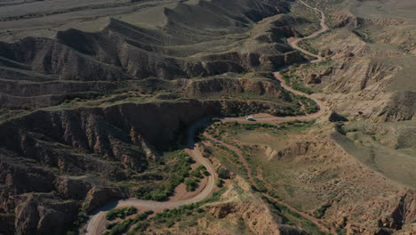 Picturesque-aerial-view-of-a-car-traveling-along-a-winding-road-through-Fairytale-Canyon-in-Kyrgyzstan