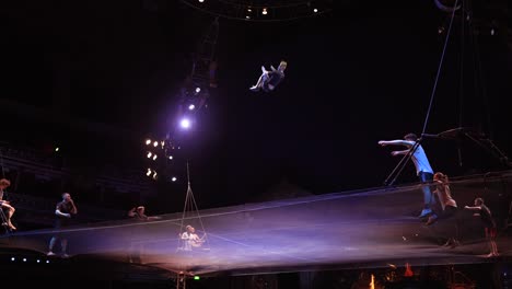 Cirque-Du-Soleil:-Atletas-De-Circo-Profesionales-Practicando-Y-Ensayando-El-Acto-De-Trampolín-En-Un-Impresionante-Lugar-Con-Luz-Tenue,-Hombre-Cayendo-De-Una-Escalera-De-Cuerda