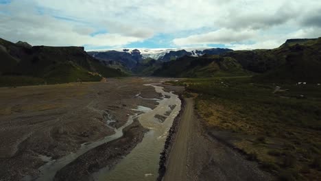 Aerial-landscape-view-of-a-river-flowing-through-a-valley,-next-to-a-road,-in-the-Fimmvörðuháls-area,-Iceland