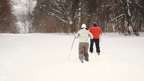 Couple-on-vacation-hiking-through-the-deep-snow-in-nature-near-the-trees-and-forest,-leisure-and-free-time-activity-concept