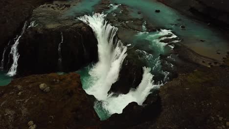 Aerial-drone-view-above-river-water-flowing-down-a-large-waterfall,-in-Iceland
