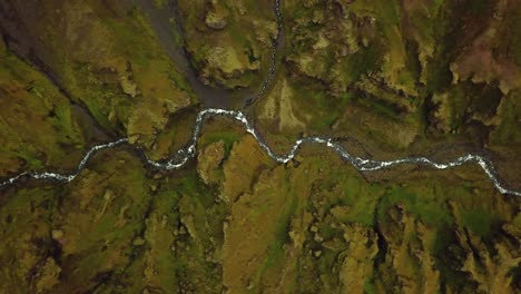 Vista-Superior-Aérea-Sobre-Un-Río-Que-Fluye-Y-Texturas-Y-Patrones-Naturales-Del-Terreno-Islandés