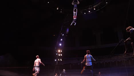 Cirque-Du-Soleil:-Atletas-De-Circo-Profesionales-Practicando-Y-Ensayando-El-Acto-De-Trampolín-En-Un-Impresionante-Lugar-Con-Luz-Tenue,-Hombre-Cayendo-Del-Trapecio