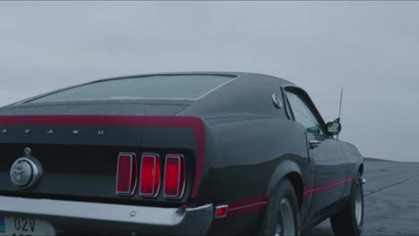 Back-of-Ford-Mustang-Mach-1-Classic-Sports-Car-Moving-on-Wet-Road-and-Rainy-Day