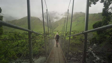 Woman-hiking-with-nordic-walking-poles-across-suspension-bridge-on-Rob-Roy-Glacier-Trail