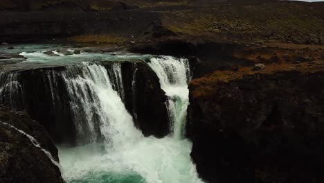 Aerial-drone-view-over-water-flowing-down-a-large-waterfall,-in-Iceland
