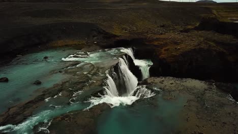 Aerial-drone-view-over-river-water-flowing-down-a-large-waterfall,-in-Iceland