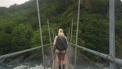 Female-adventure-backpacker-crossing-suspension-bridge-during-nature-trail-in-New-Zealand