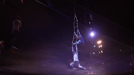 Cirque-Du-Soleil:-Professionelle-Zirkussportler-üben-Und-Proben-Trampolin-Darbietungen-In-Einem-Atemberaubenden-Ort-Mit-Gedimmtem-Licht,-Zwei-Männer-Werden-Von-Einer-Strickleiter-Hochgehoben-Und-Fallen
