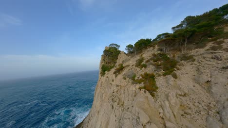 FPV-Drone-flying-over-rocky-cliffs-in-Mallorca-and-through-trees-towards-the-great-ocean