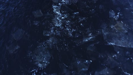Large-ice-blocks-floating-in-dark-deep-water,-aerial-downwards-view
