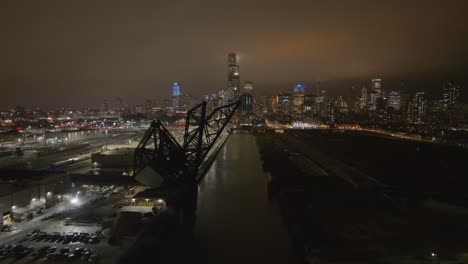 Aerial-view-over-a-rail-line-bridge,-revealing-the-Amtrak-Train-Station-and-the-hazy,-Chicago-night-skyline