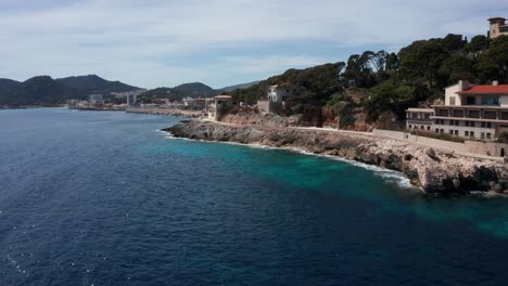 Drone-Shot-Cala-Rajada-Harbour-in-Mallorca-with-clear-blue-water-with-mountains-and-hills-in-the-background