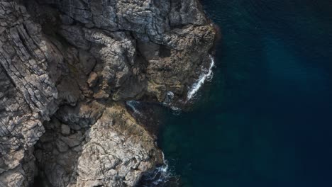 Drone-Top-Down-Shot-on-Rocky-Cliffside-with-waves-crashing-onto-it