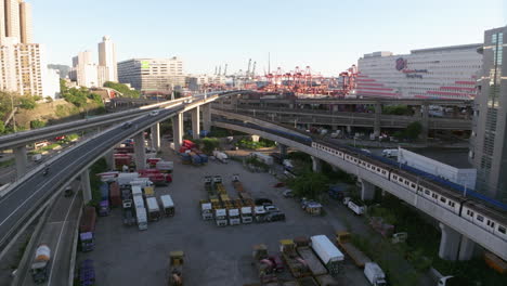 Luftaufnahme-Nach-Vorne-Von-Tsuen-Wan-Line-MTR-Zug-Und-Industriehafen-Mit-Kränen-Im-Hintergrund---Hongkong,-Asien