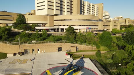 Modern-helicopter-near-University-of-Michigan-Hospital,-aerial-ascend-view