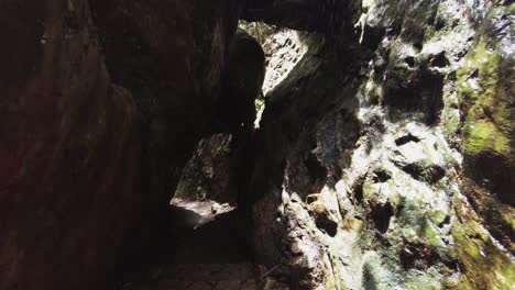 Walking-Through-Narrow-Rock-Tunnel-With-Waterfall,-POV-Dolly