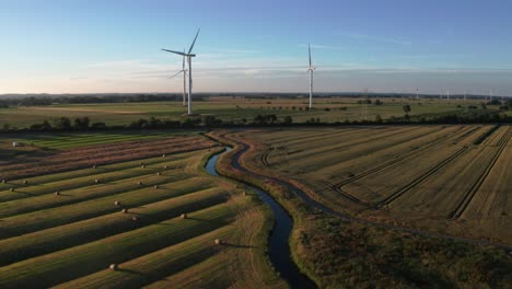 Drone-shot-Wheat-field-with-wind-turbines-at-golden-hour-with-blue-skies-and-a-small-river