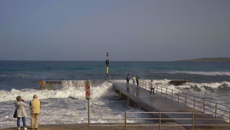 Ocean-waves-breaking-at-a-stone-peer-on-Mallorca-with-big-splashes-an-people-on-the-peer