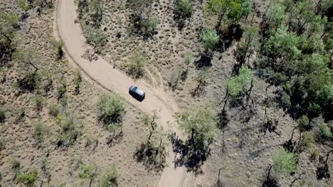 Top-down-shot-of-an-SUV-driving-through-Australia's-dry-countryside-on-a-dirt-road