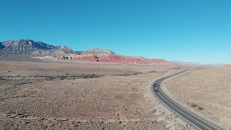 Aerial-drone-shot-of-Red-Rock-Scenic-Highway-with-mountains-in-the-background