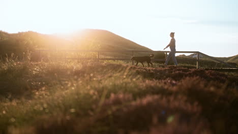 Woman-walks-with-her-dog-while-sunset-in-a-national-park