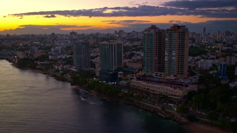 Aerial-drone-view-over-seafront-skyscrapers-along-Malecon-at-sunset,-Santo-Domingo-in-Dominican-Republic