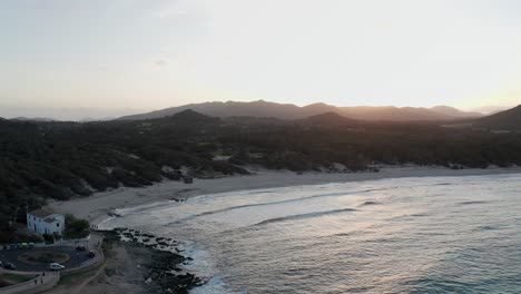 Mallorca-beach-Cala-Aguila-at-sunset-on-a-warm-evening-with-waves-crashing-onto-beach-and-the-sun-setting-behind-distant-mountains