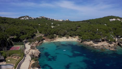 Mallorca-Cala-Gat-Playa-Con-Agua-Azul-Clara-En-Un-Día-Soleado-Con-Surfista-En-El-Agua-Y-Montañas-En-El-Fondo