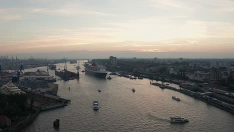 Drone-Shot-Hamburg-Harbour-Queen-Mary-2-entering-the-harbour-during-sunset-golden-hour-at-cruise-days-with-skyline-in-the-background
