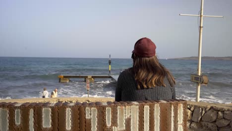 Pregnant-woman-with-a-red-hat-watches-the-ocean-waves-on-Mallorca