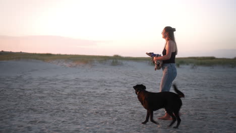 Woman-walks-her-dog-barefoot-on-the-beach-while-sunset