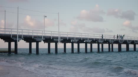 A-sturdy-built-pier-stretches-across-the-chilly-beach-water-as-it-reflects-the-blue-and-pink-pastel-colours-of-the-light-spilling-from-a-setting-sun