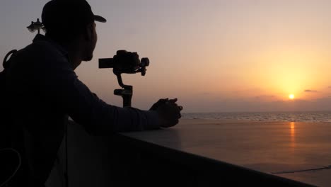 Silhouette-Des-Fotografen-Und-Der-Dslr-kamera,-Die-Den-Orangefarbenen-Sonnenuntergang-über-Dem-Ozean-Filmen