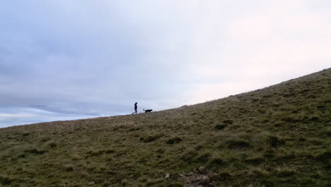 Drone-shot-of-a-woman-and-her-dog-walking-on-the-top-of-a-mountain-range