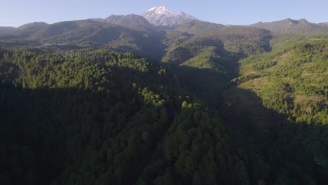 Drone-video-of-a-highway-across-the-forest-in-the-hills-near-the-Pico-de-Orizaba-volcano,-with-the-volcano-in-the-background