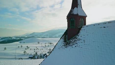 Drone-footage-flying-over-a-tiny-chapel-and-an-idyllic-wintry-landscape-in-rural-Switzerland