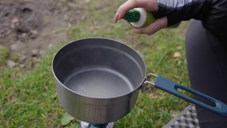 oiling-the-pot-on-the-field-cooker-at-the-bank-of-the-loch-during-a-day,-food-preparation