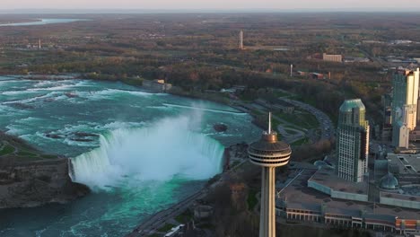 Niagara-falls-from-Canada-side-with-observation-tower-during-sunset,-Drone-descending-and-orbiting